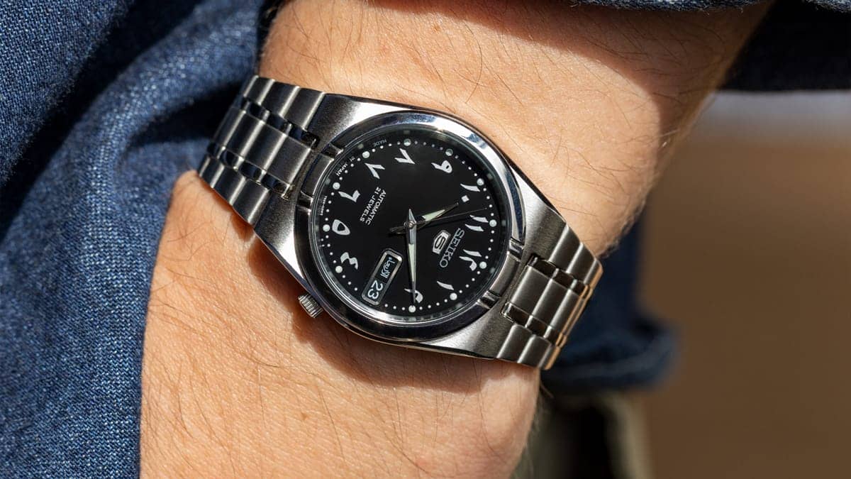 Seiko 5 automatic black Arabic numeral dial stainless steel bracelet worn on wrist close-up date window everyday wear price guide 2026